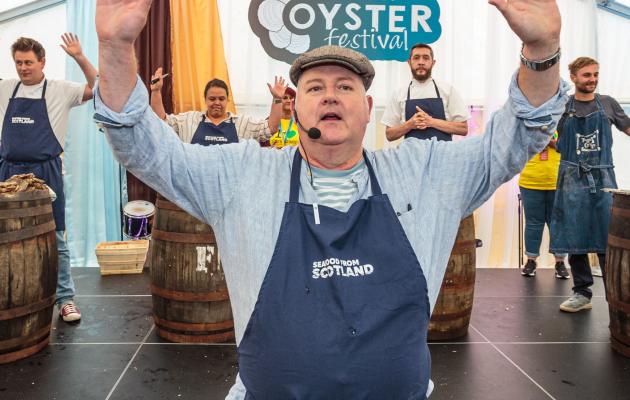 A man standing with hands raised with oyster shuckers in the background